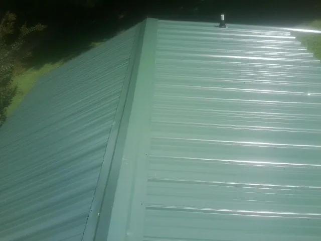 New green metal panels meeting at the ridge of a roof — Flat Roof Repair work by our crew in Brunswick